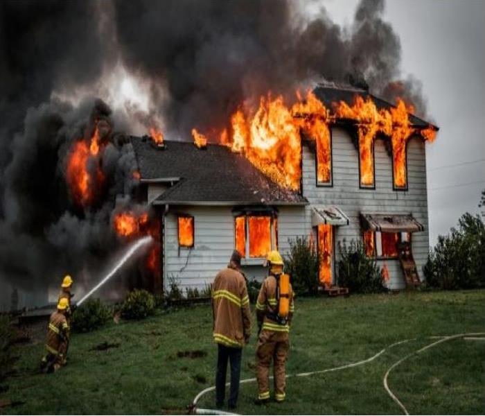 Fire fighters stand in front of a burning home
